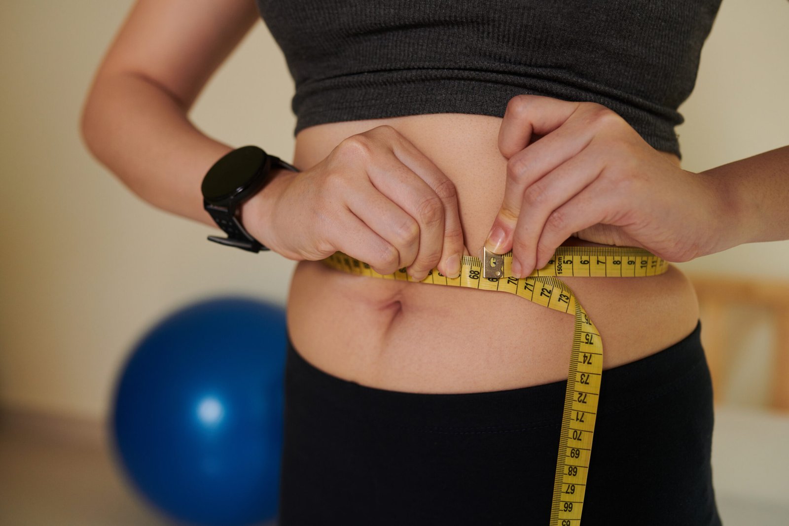 Cropped image of young woman measuring her waist after training at home, healthy lifestyle and loosing weight concept