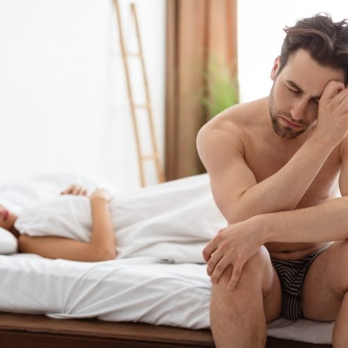 Erectile Dysfunction Issue. Depressed Guy Having Problems With Erection While His Wife Lying In Bed Indoors. Male Health And Stress, Sexual Failure And Impotence Concept. Selective Focus