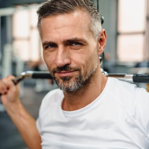 Attractive confident healthy sports man using seated lat pulldown machine in the gym, close up