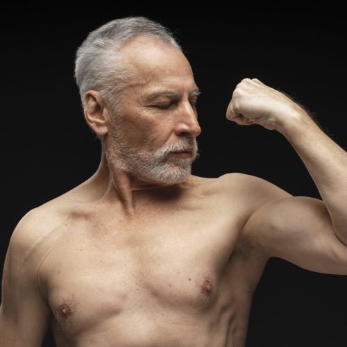 Portrait of attractive serious senior man, athlete showing biceps, muscular body isolated on black background. Advertisement concept