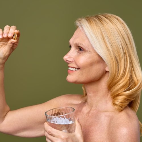 A smiling mature woman holds a supplement and a glass of water, advocating for healthy lifestyle choices and wellness. She exudes positivity and vitality