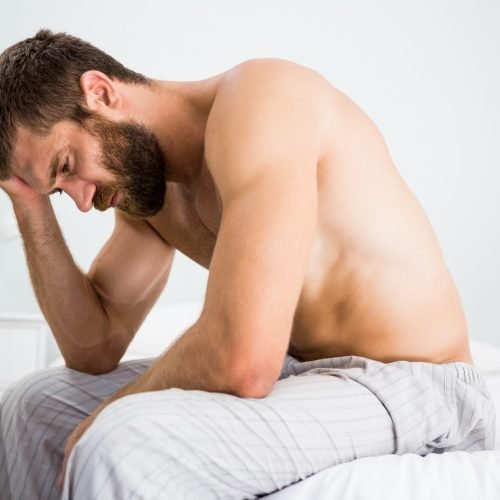 Depressed man on bed with hand on head at bedroom