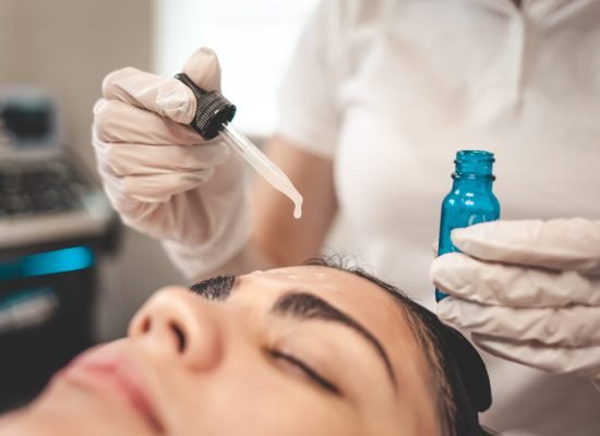 Doctor beautician applies oil to the skin of the face