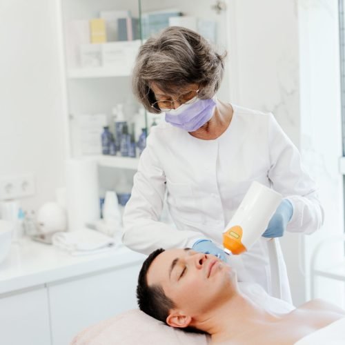 Professional, senior woman, doctor cosmetologist using laser, facial skin treatment, acne, rejuvenation, work in modern cosmetic clinic. Cosmetology concept, cosmetic procedure