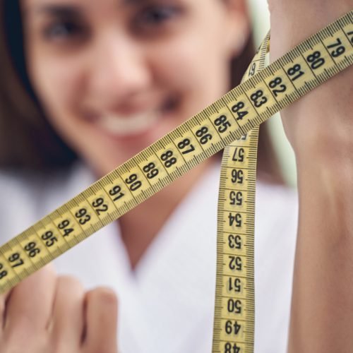 Close up of female hands holding tape measure or flexible ruler for measuring size or distance