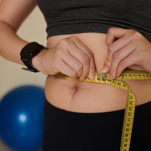 Cropped image of young woman measuring her waist after training at home, healthy lifestyle and loosing weight concept