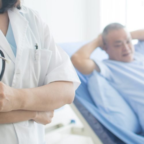Healthcare and medical concept, close up doctor holding stethoscope with old patient laying down on bed