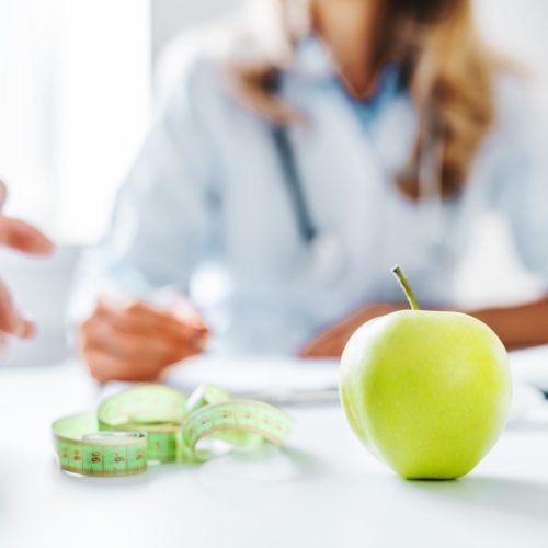 Healthy food concept. Cropped close up of woman doctor dietician recommending senior male patient fresh apple