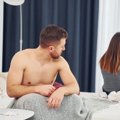 Disappointed woman sitting on the bed with back to the man that feels bad.