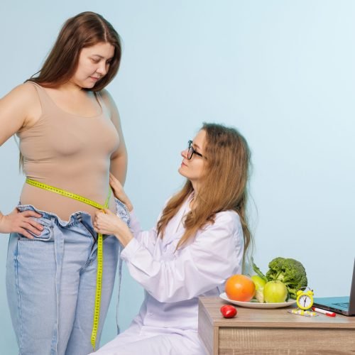 Nutritionist measuring waist of plus size woman during weight loss consultation for healthy lifestyle and wellness